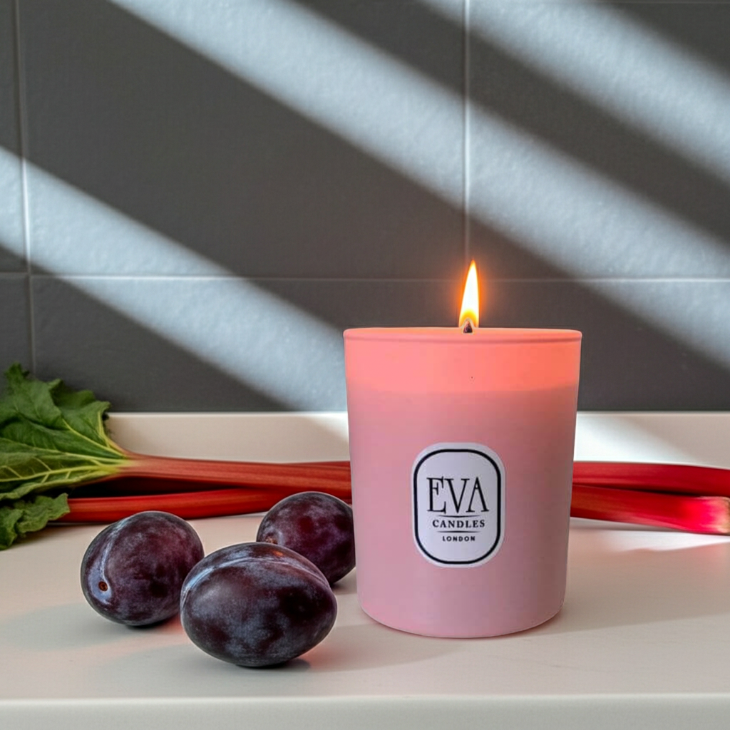 Pink candle with 'EVA CANDLES LONDON' label on a surface with plums and rhubarb. 