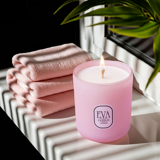 Pink candle with 'EVA CANDLES' label on a reflective surface with towels and a plant in the background